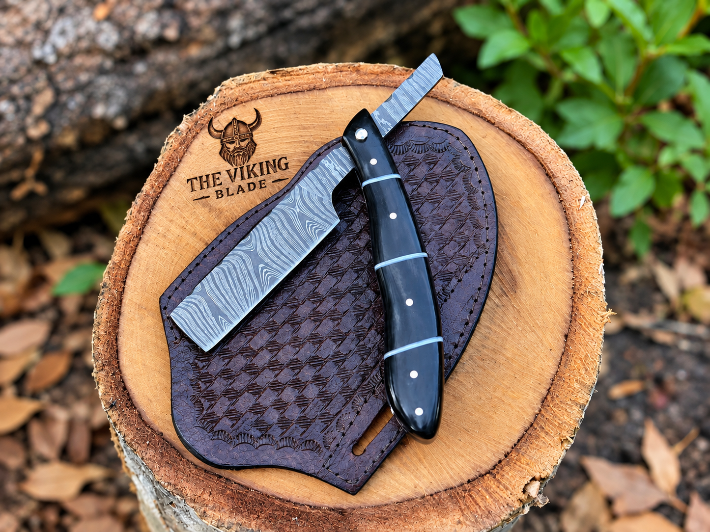 The Viking Blade Damascus folding razor features layered steel, a sharp edge, elegant craftsmanship, and a genuine leather sheath—perfect for collectors.