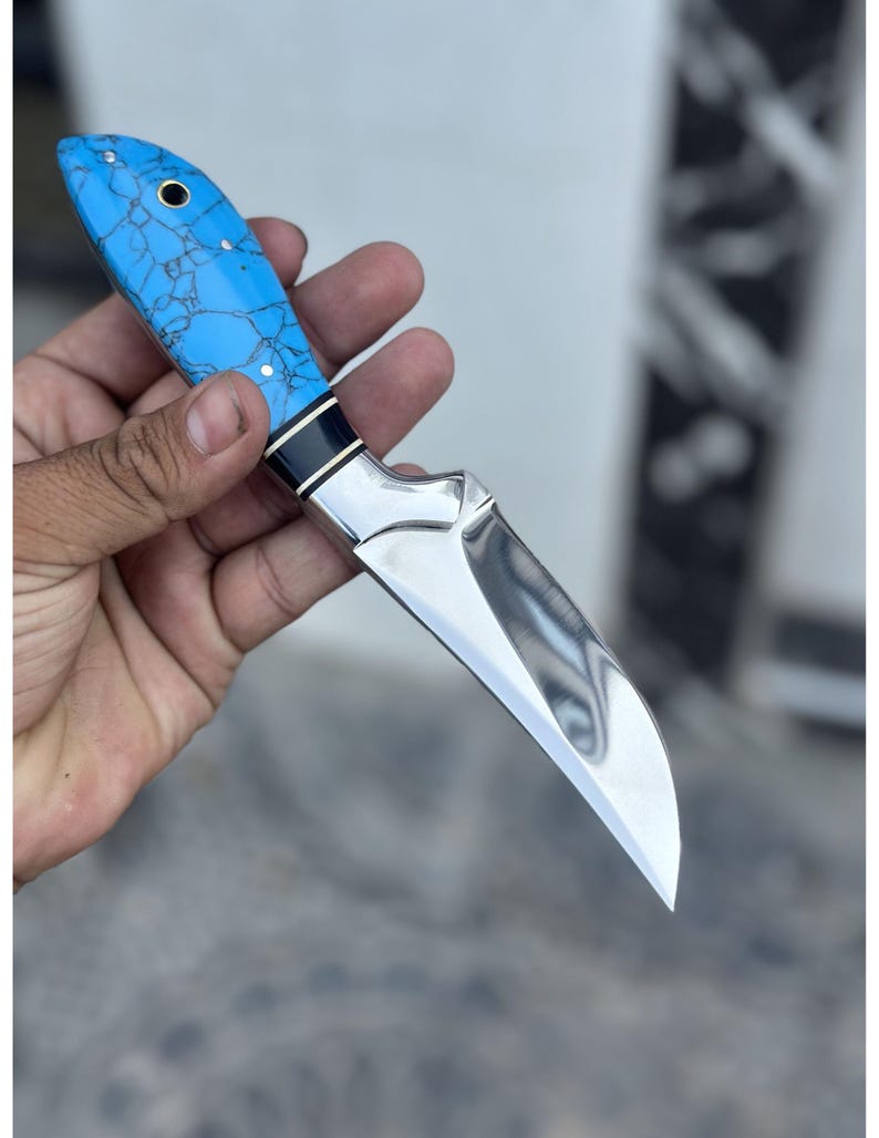 Hand holding a knife with a blue handle against a blurred background