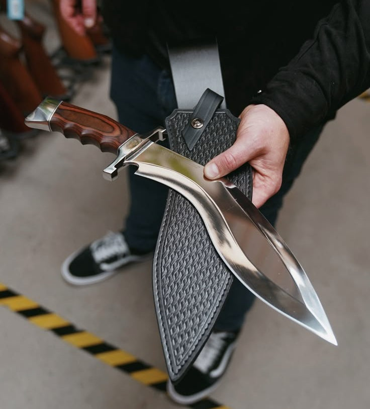 Person holding a kukri knife with a sheath on a blurred background