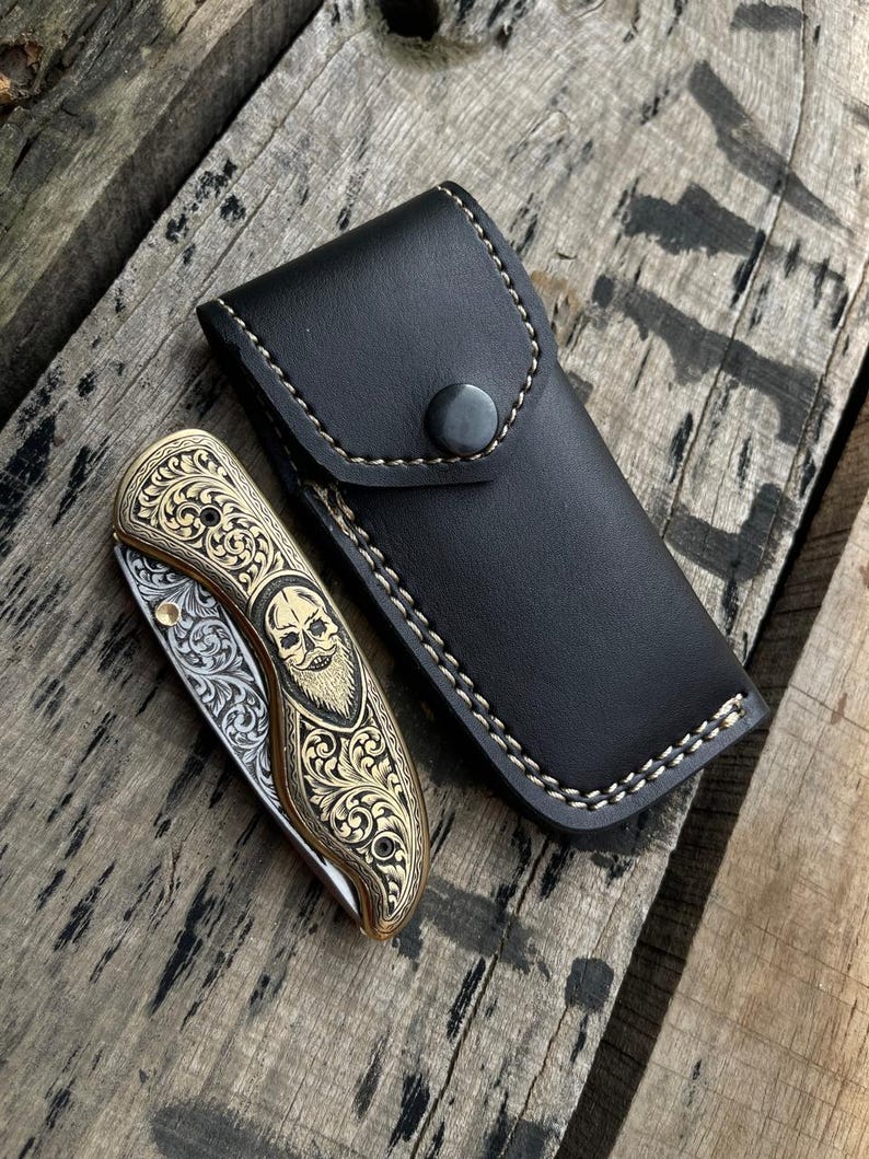 Decorative pocket knife with black leather sheath on wooden surface
