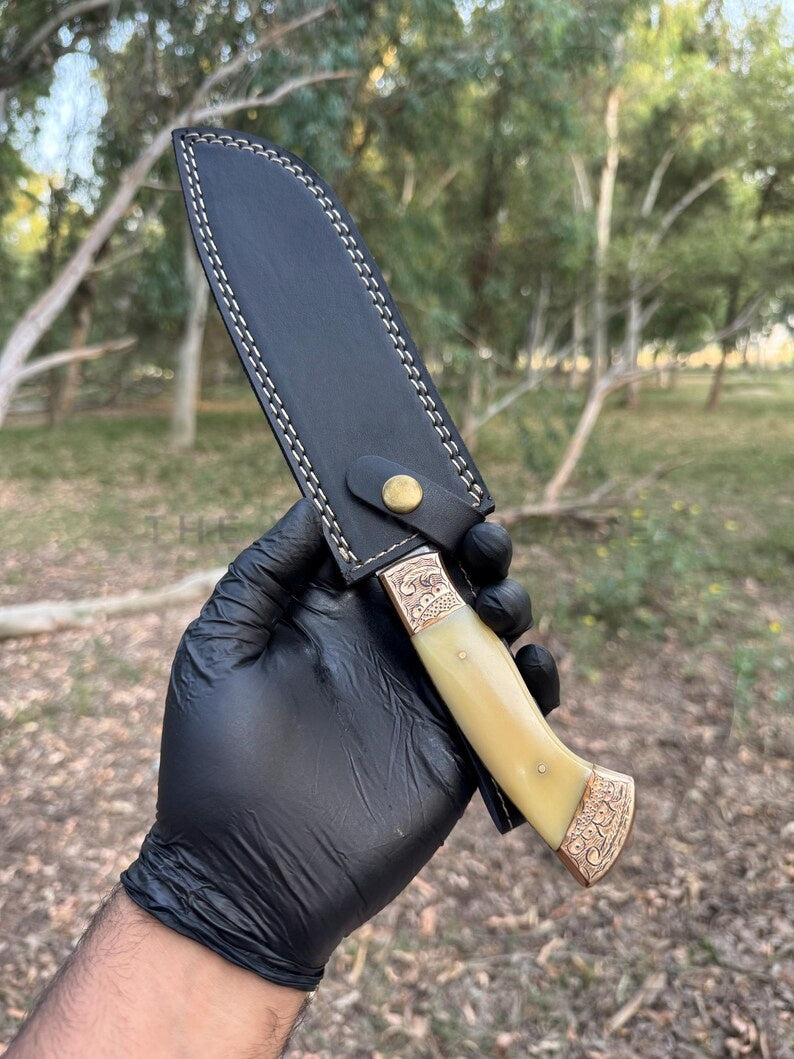 Knife with decorative handle held by a gloved hand against a natural background