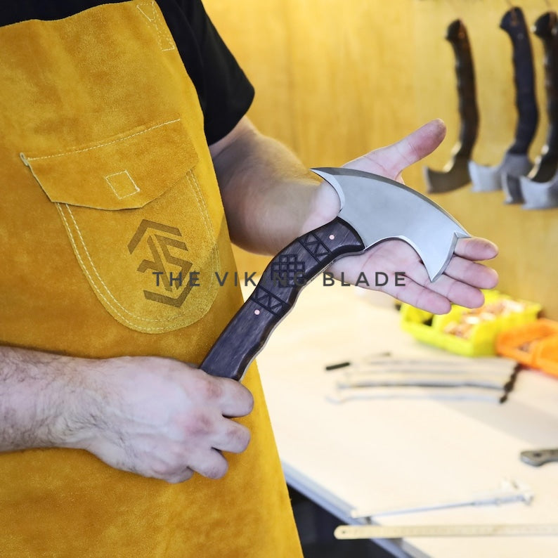Person holding a Viking-style axe with 'The Viking Blade' branding, wearing a yellow apron.