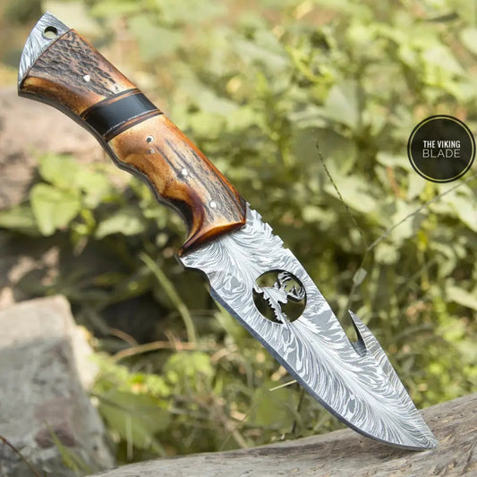 An 11-inch custom hand forged Damascus steel full tang skinner knife with a Gut hook and a stag handle, displayed outdoors with a leather sheath.