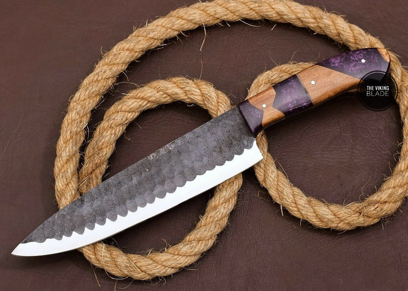 A custom hand forged D2 steel knife with a wood and resin handle, featuring a shard blade design, displayed next to a leather sheath, against a backdrop of a twine-wrapped rope.