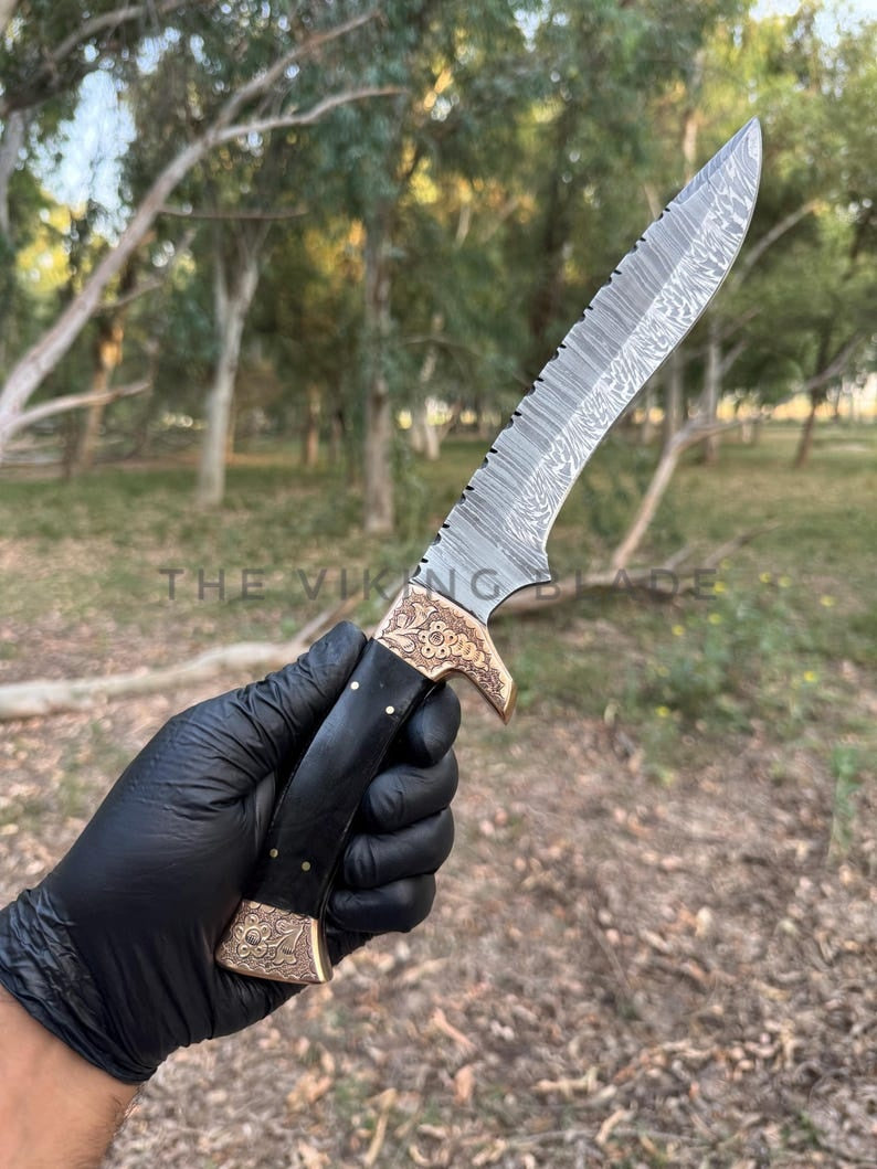 Hand holding a dagger with a detailed handle in a natural setting