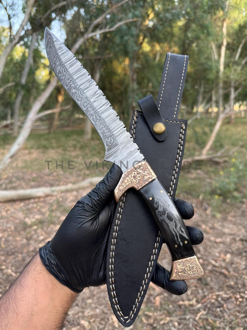 Decorative knife with sheath held by a gloved hand, outdoors.