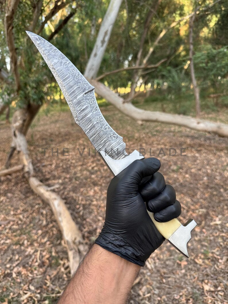 Knife with a textured blade held by a person wearing a black glove, outdoors.