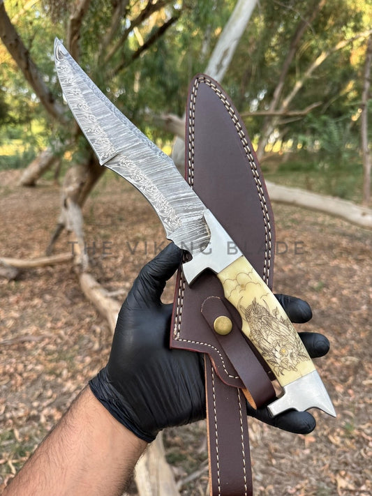 Knife with leather sheath held by a gloved hand in a forest setting