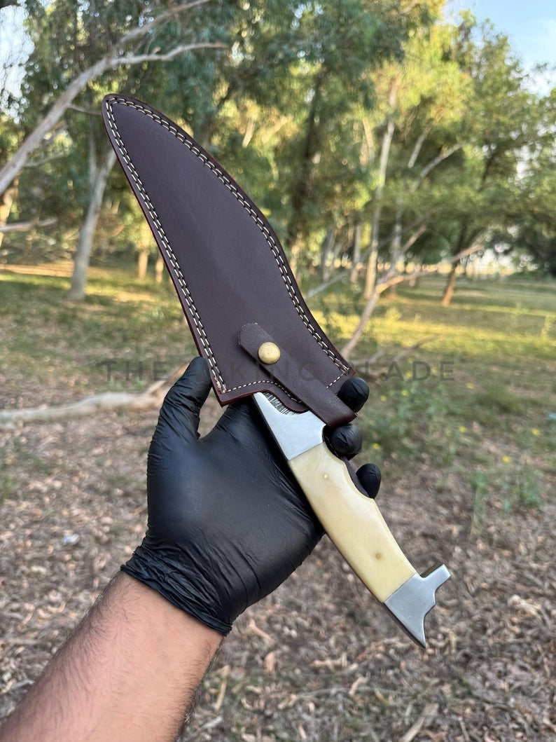 Hand holding a knife with a leather sheath outdoors