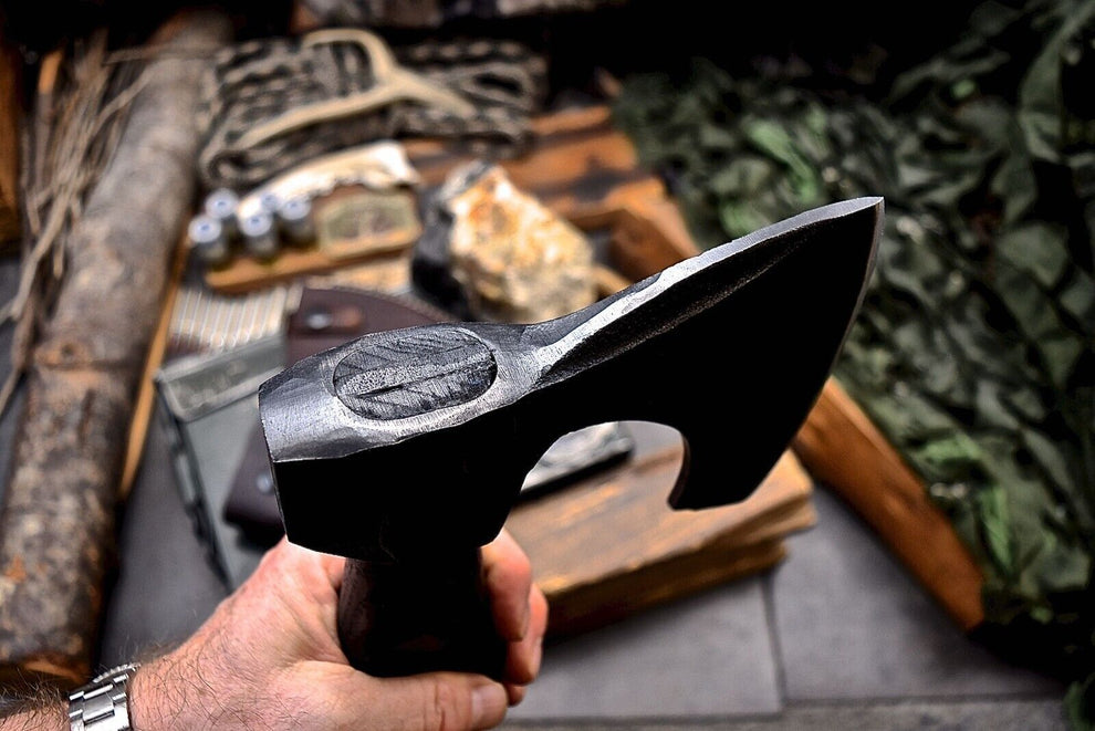 Hand holding a black axe with a blurred natural background