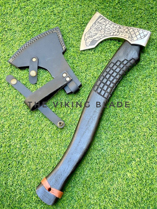 Decorative axe with patterned blade and textured handle on grass, branded 'The Viking Blade'.