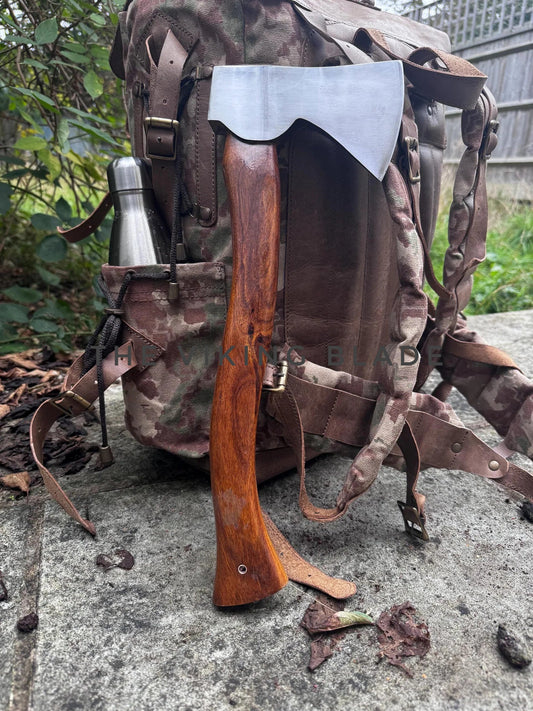 Camouflage backpack with axe and thermos on a concrete surface