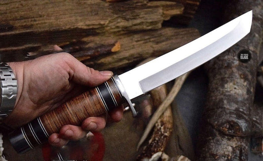 A hand forged D2 steel tanto knife with a white micarta handle and a cow leather sheath, being held by a person.