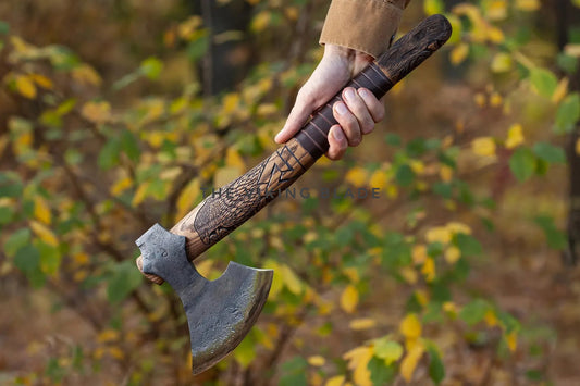 Hand holding a decorative axe against a blurred natural background