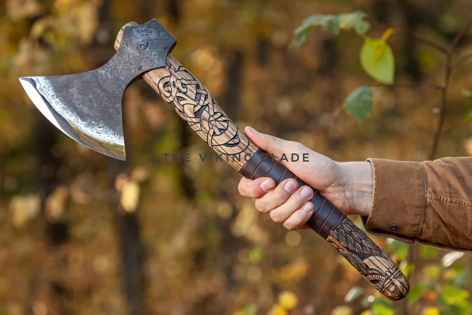 Hand holding a decorative axe with a blurred natural background