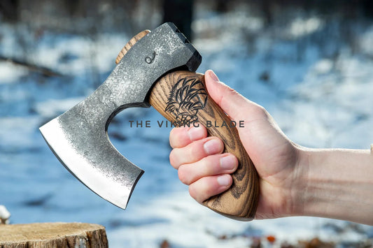 Hand holding a axe with 'The Viking Blade' branding against a blurred natural background