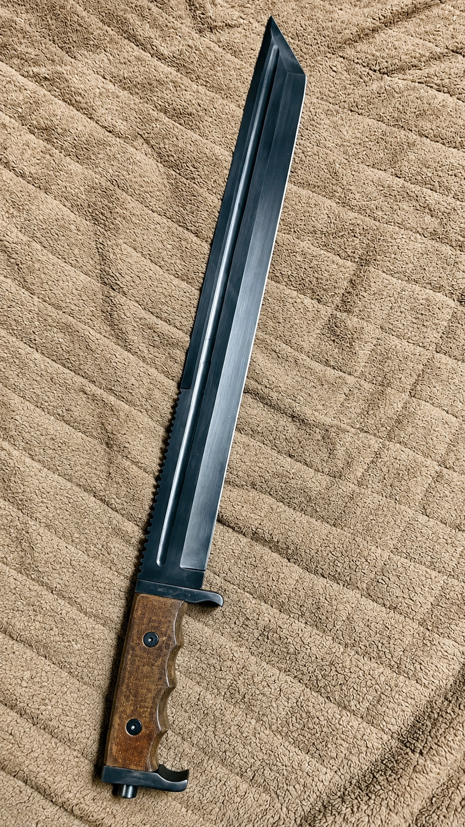 A fixed-blade knife with a long black metal blade and a brown wood-grain handle, laid diagonally on a beige textured blanket.