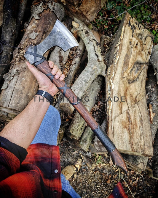 Person holding a axe over chopped wood with 'The Viking Blade' branding.