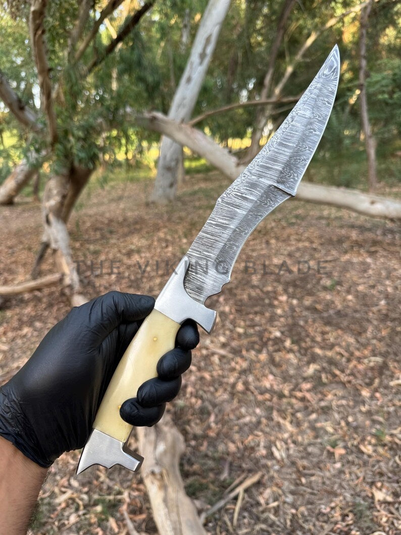 Knife with a wooden handle held by a person wearing black gloves, outdoors.