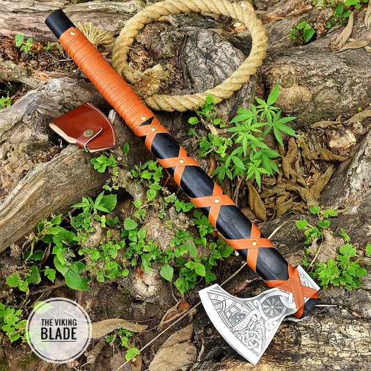 A hand forged high carbon steel tomahawk axe with a leather sheath and a rope, placed on a bed of wooden logs and green moss.
