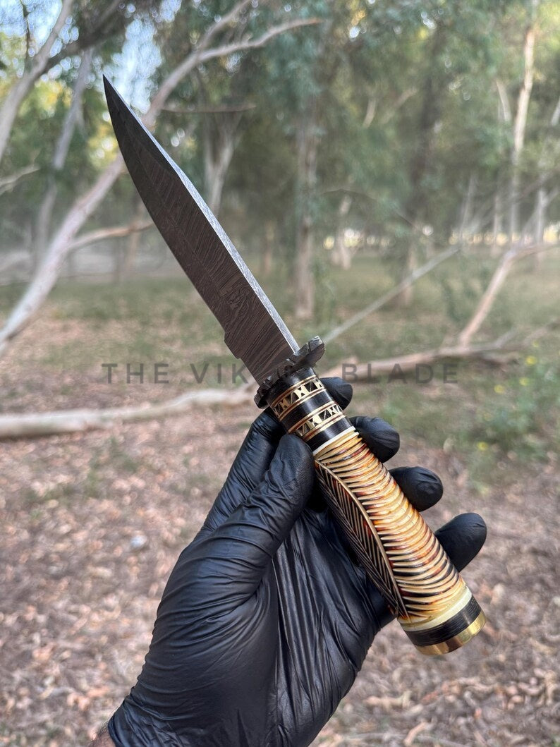 Knife with a decorative handle held by a gloved hand against a natural background
