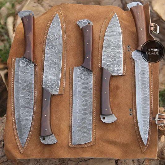 A set of custom hand forged Damascus steel kitchen knives with wood handles, displayed on a leather pouch background, including paring, bread, utility, chef, and cleaver knives.