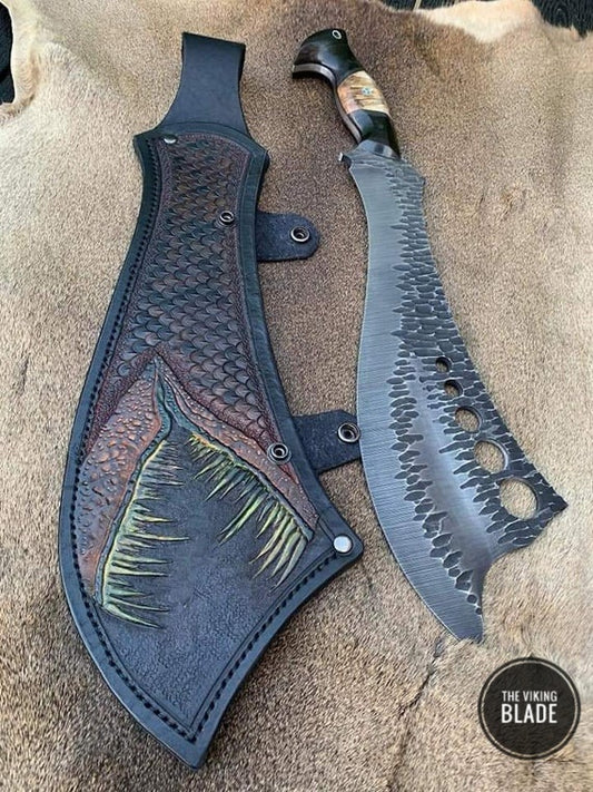 A hand forged survival knife with a black leather handle and a patterned blade, accompanied by a brown leather sheath cover.
