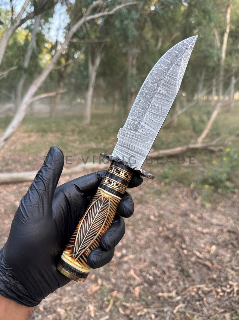 Hand holding a decorative knife with a detailed handle in an outdoor setting