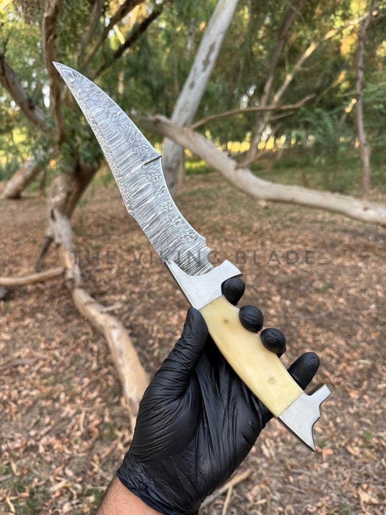 Knife with a decorative blade held by a person wearing a black glove in a forest setting.