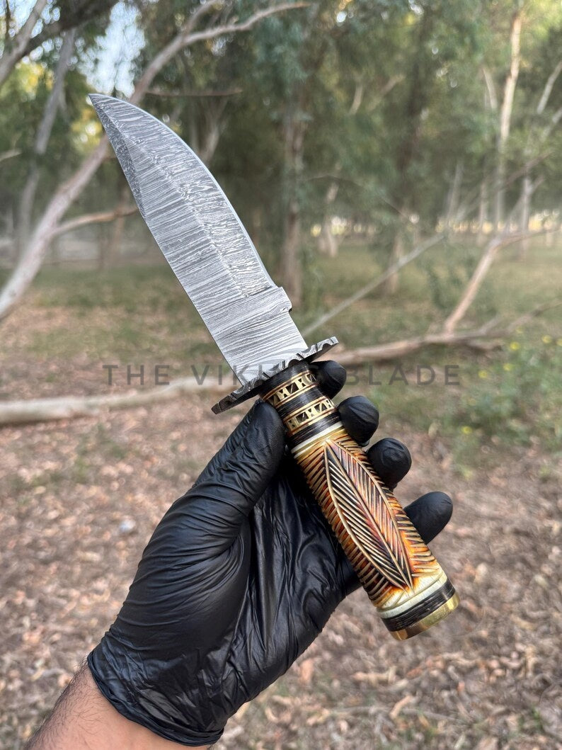 Hand holding a knife with a decorative handle in a natural setting