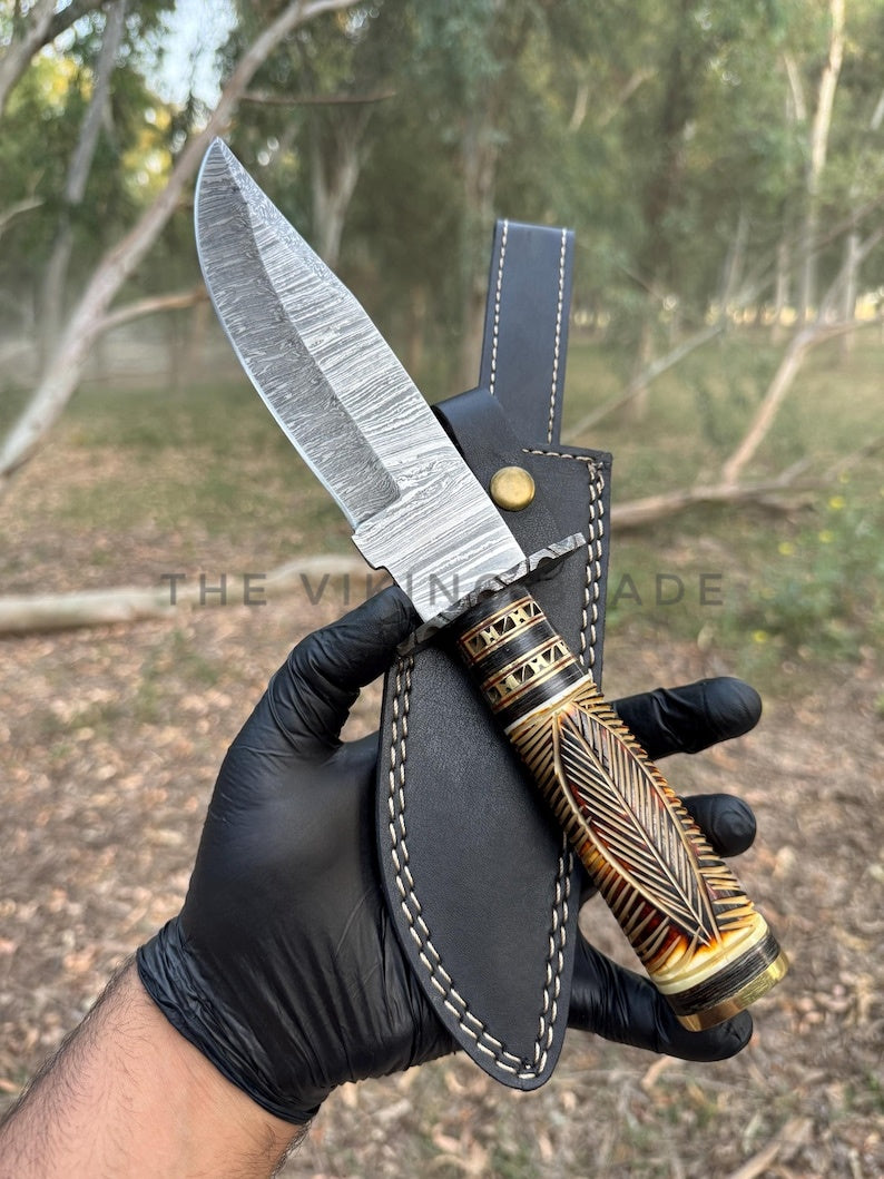 Knife with decorative handle held by a gloved hand against a natural background