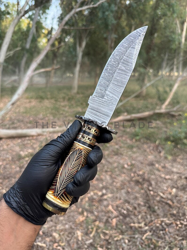 Knife with decorative handle held by a gloved hand in an outdoor setting