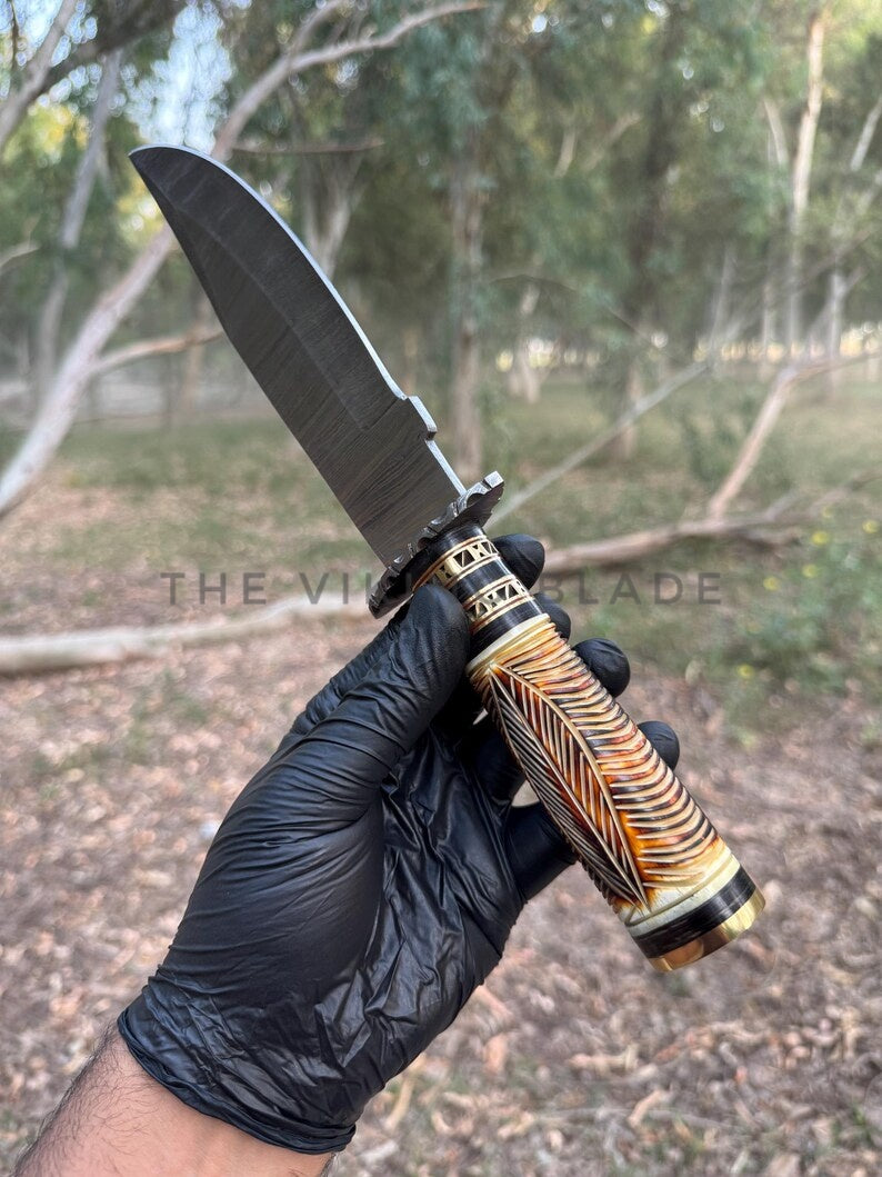 Knife with decorative handle held by a gloved hand against a natural background