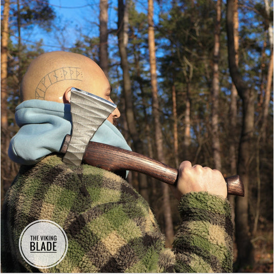 A person holding a hand forged hatchet with a leather sheath, standing in a forest.
