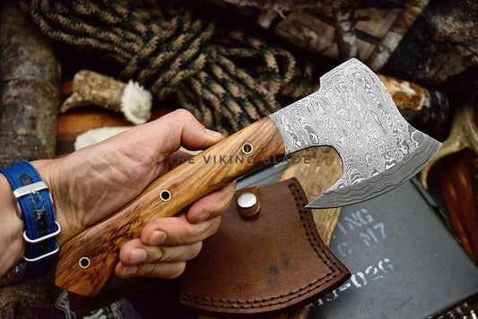 Hand holding a Viking-style axe with a leather sheath, surrounded by natural elements.