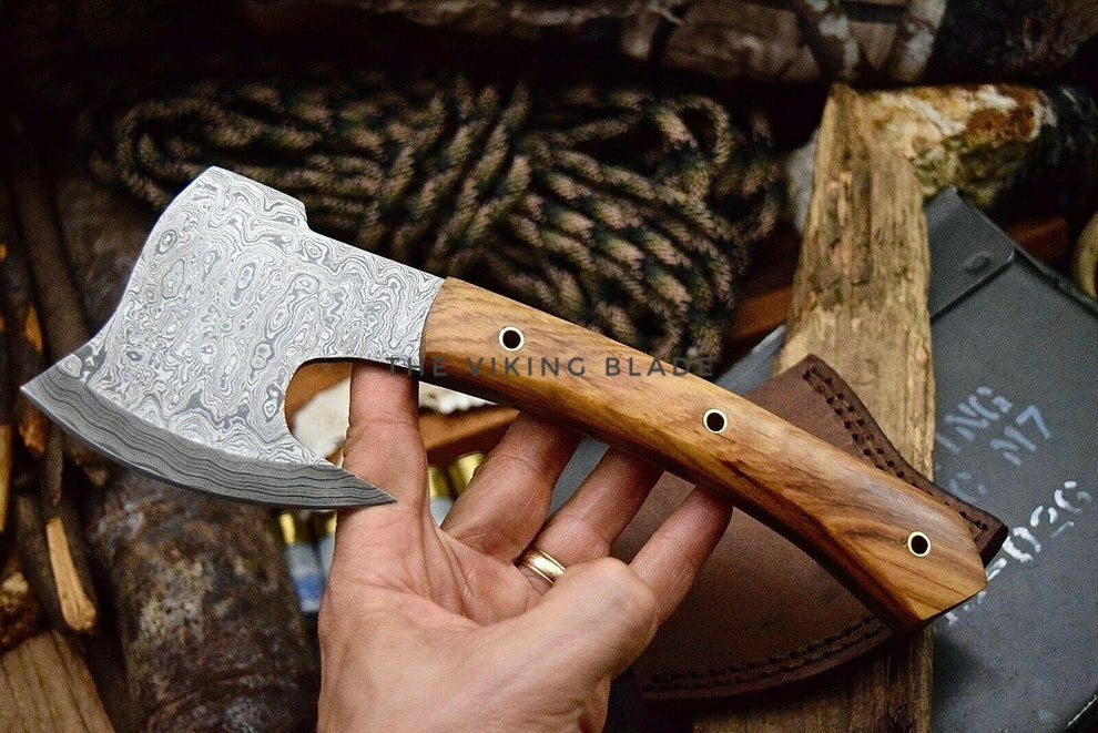 Hand holding a decorative axe with a wooden handle against a rustic background