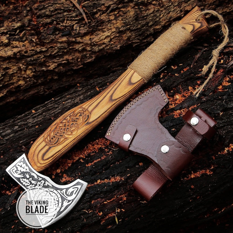 A handcrafted carbon steel Viking style axe with a wooden handle and a leather sheath, placed on a wooden surface.