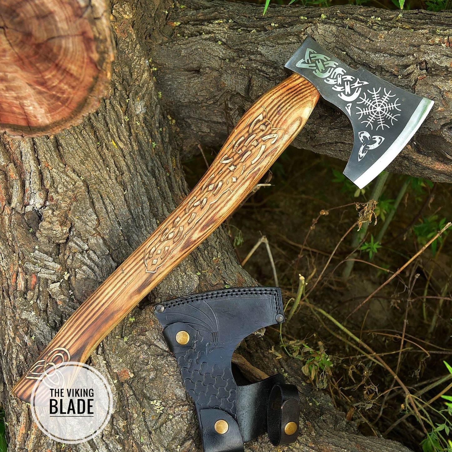 A hand forged carbon steel Viking axe with a leather sheath, placed against a natural outdoor background.