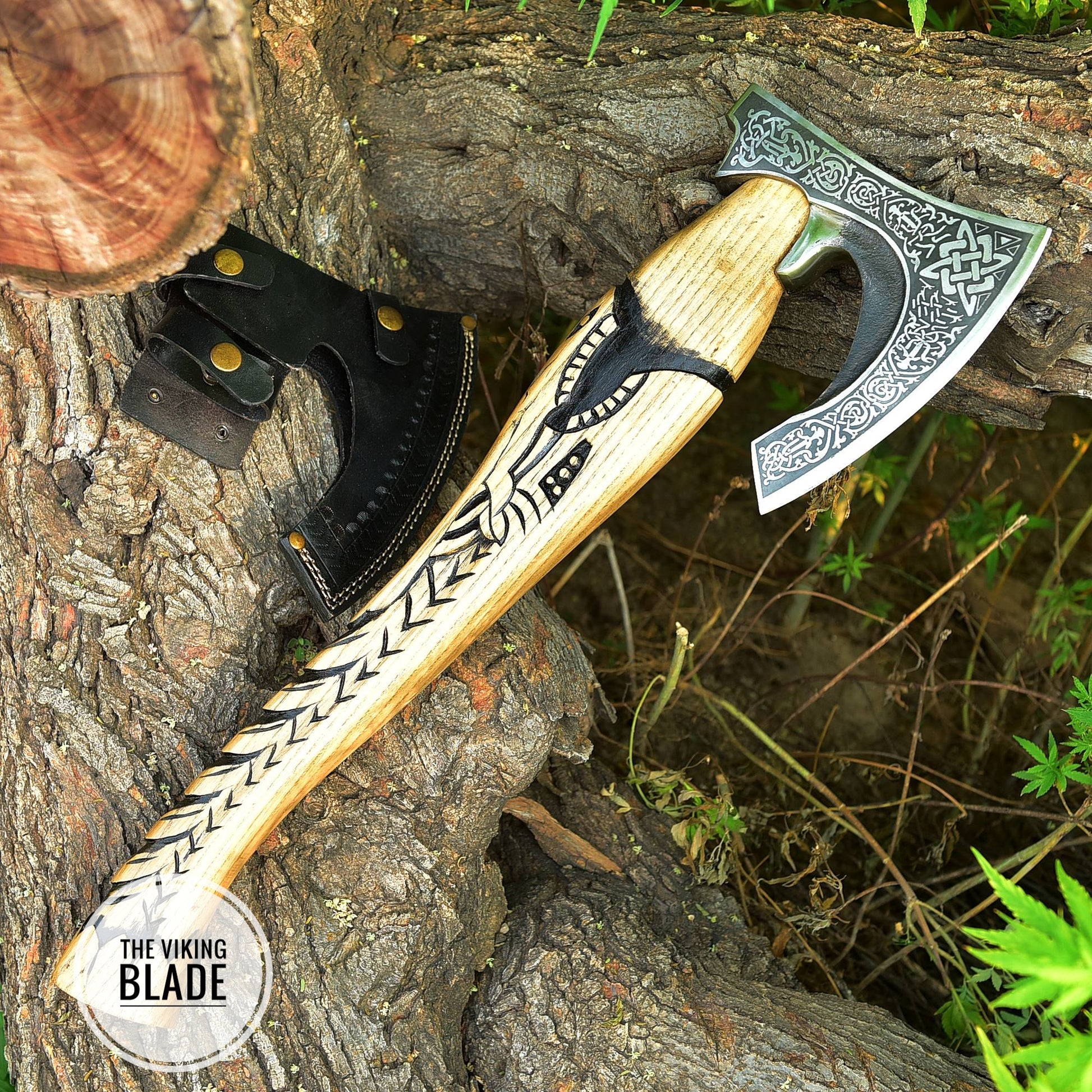 A handmade carbon steel Viking axe with a wooden handle and a leather sheath, placed against a natural outdoor background.