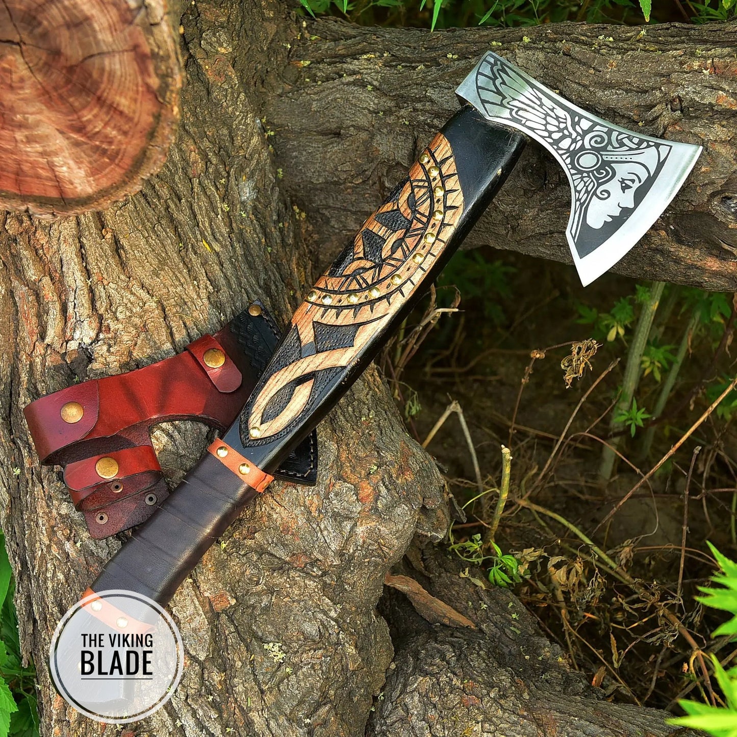 A handmade carbon steel Viking axe with a leather sheath, the axe features a decorative handle with a Viking design and a metal head, placed against a natural outdoor background.