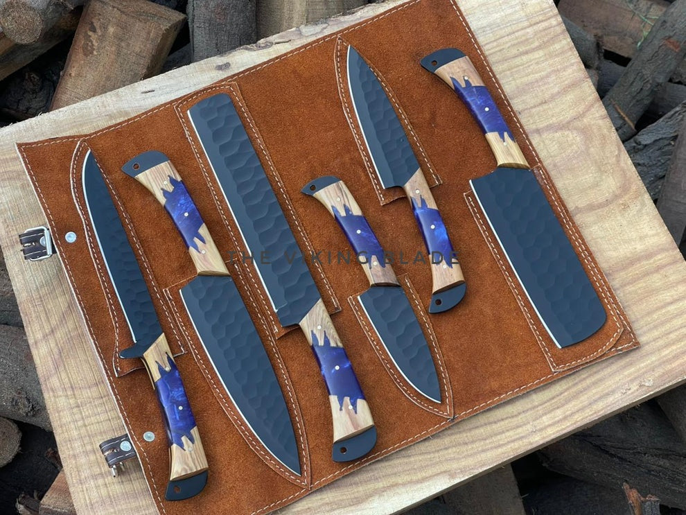 Set of knives with blue blades and wooden handles on a leather sheath.