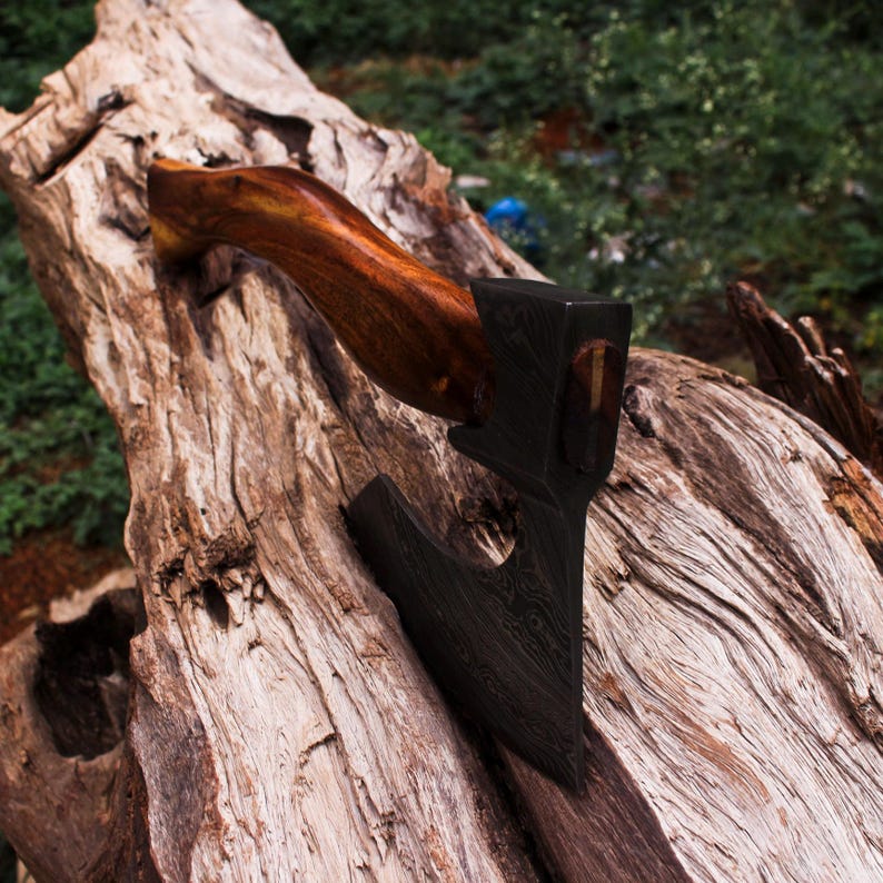 Wooden axe leaning against a large tree stump with greenery in the background
