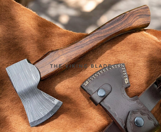 Viking-style axe with wooden handle on a brown leather surface, branded 'The Viking Blade'.