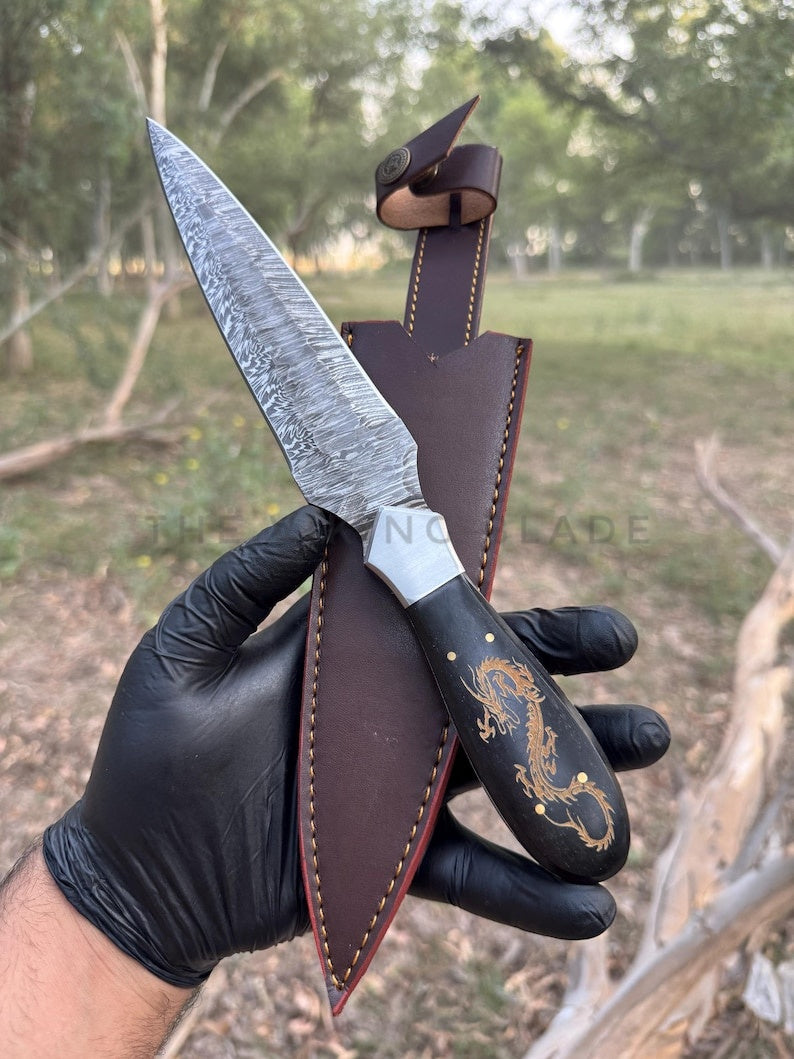 Knife with a brown leather sheath held by a gloved hand, outdoor setting