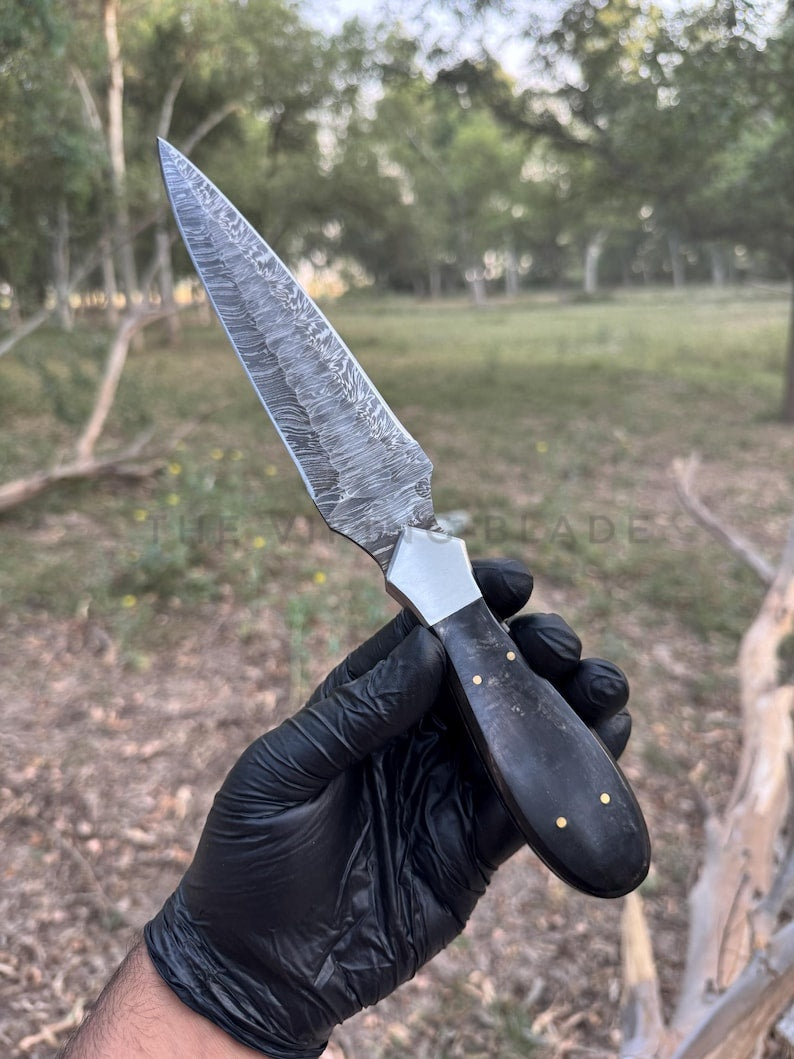 Knife held by a gloved hand with a natural outdoor background