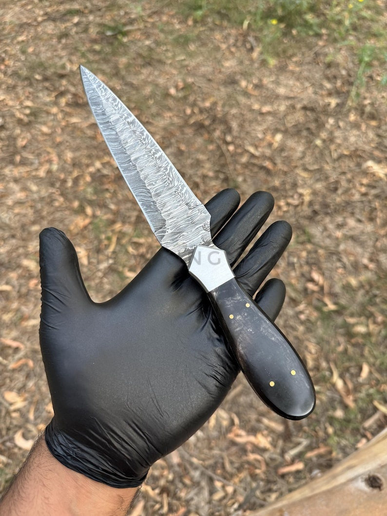 Knife with a black handle held by a gloved hand against a natural background