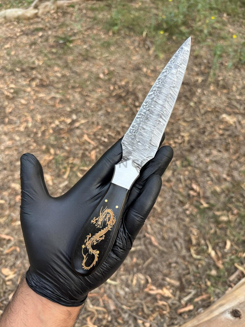 Knife with decorative handle held by a gloved hand against a natural background