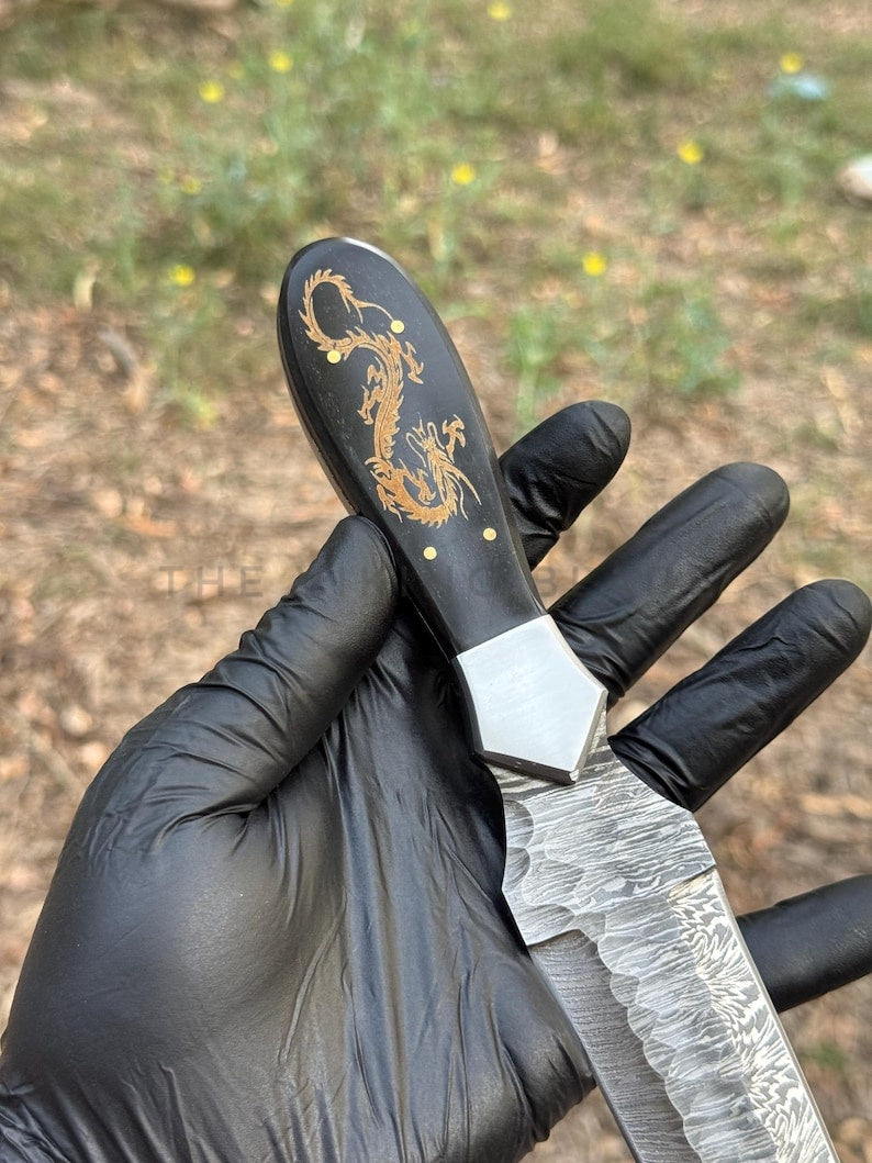 Knife with dragon design held by a gloved hand against a natural background