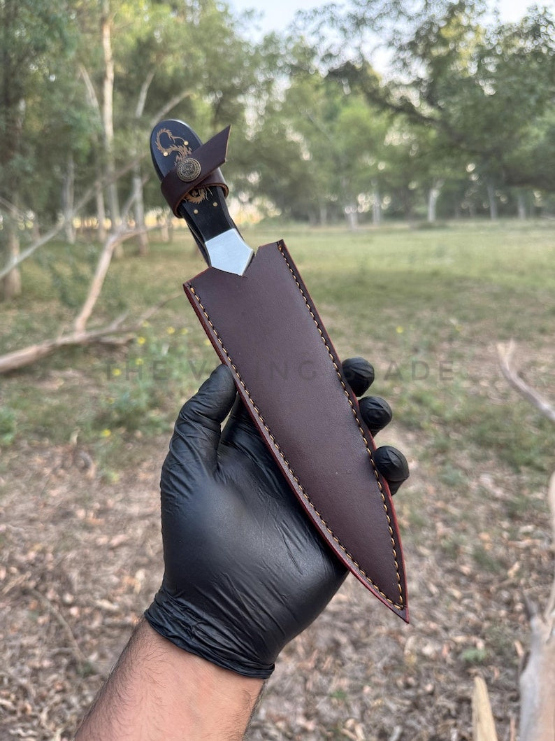 Hand holding a leather knife sheath with a forest background