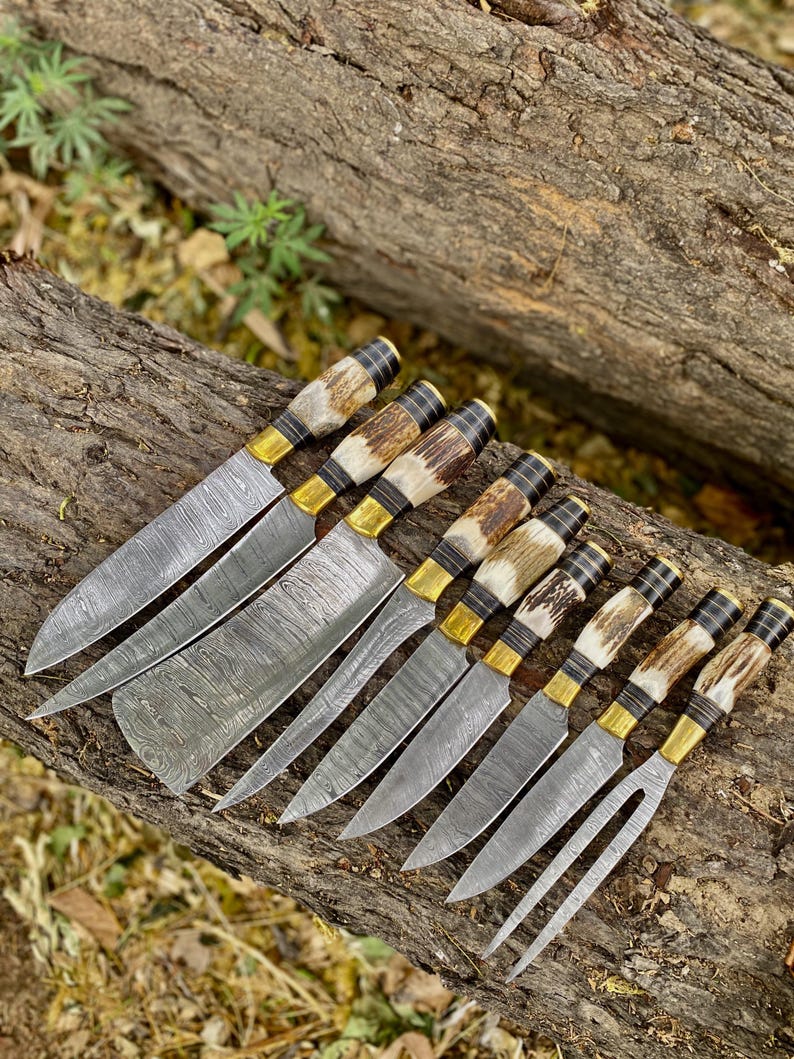 A set of custom handmade chef knives with Damascus steel blades and deer stag handle, displayed on a wooden log.